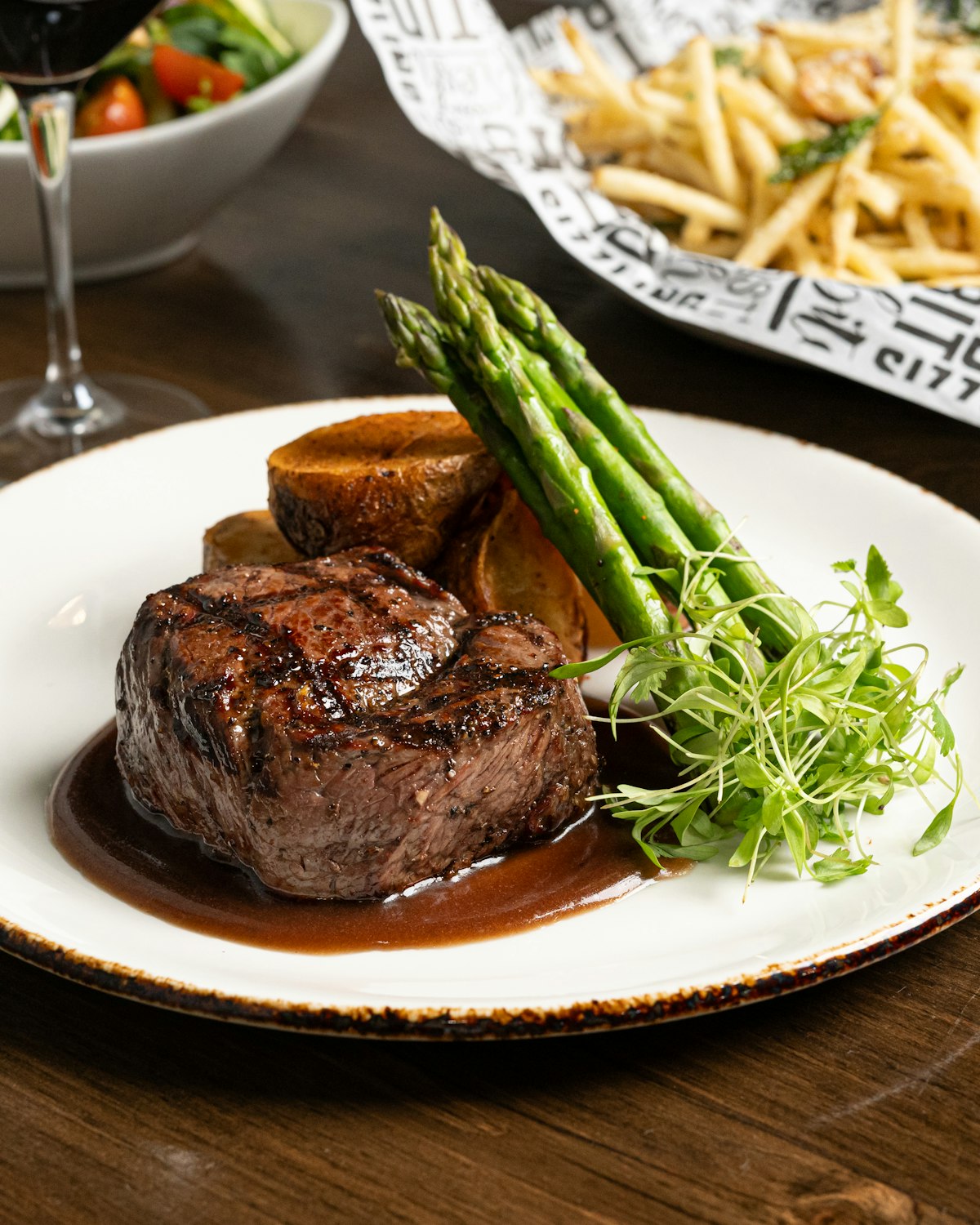 Grilled steak with asparagus, roasted potatoes and red wine jus on a white plate